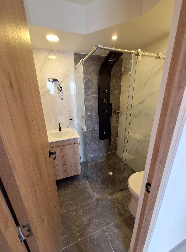 Baño con ducha en vidrio, mueble flotante y enchape combinado