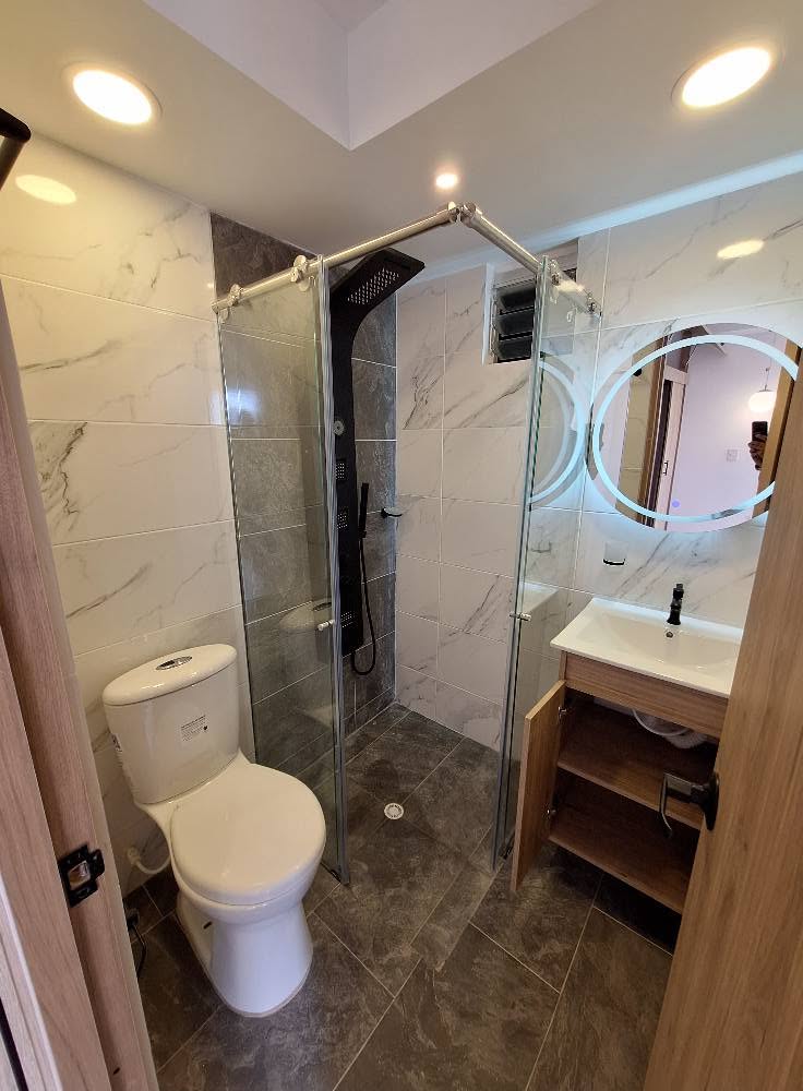 Baño remodelado con división de vidrio templado y espejo iluminado